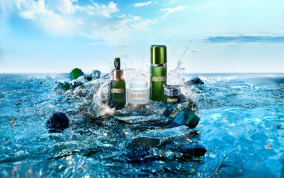La Mer skincare products displayed on wet rocks amidst splashing water under a bright sky with scattered clouds.