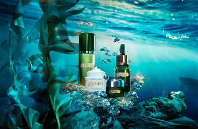 La Mer skincare products submerged in an underwater scene with green kelp fronds and rising air bubbles.