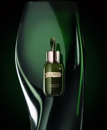 Green glass skincare bottle with silver cap positioned against a dark glossy curved green glass background.