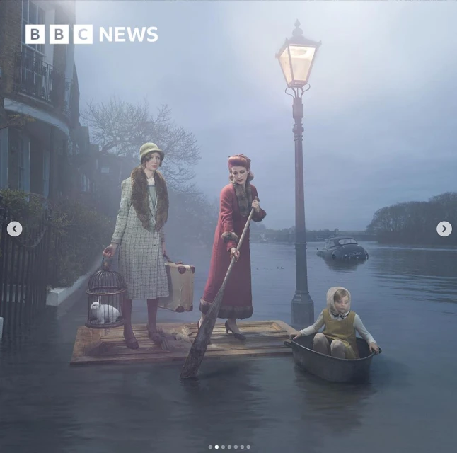 Three people in period clothing on water using a makeshift raft and rowboat, with foggy flooded street and buildings behind them.