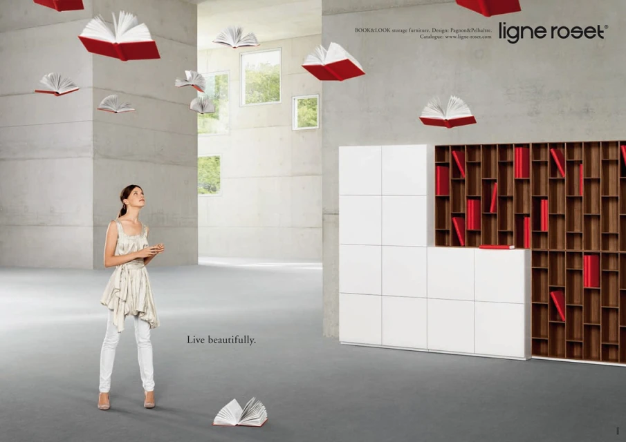 Woman in flowing top and white pants looks up at floating open books in a large studio with contemporary furniture in this promo ad.