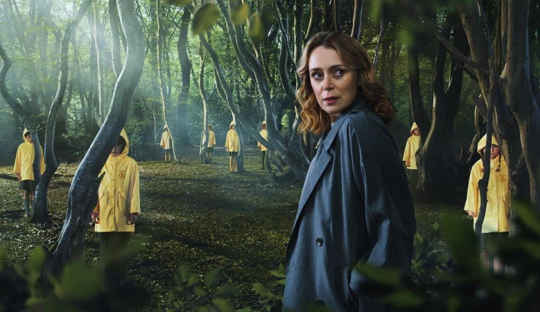 A woman in a grey coat stands in a forest clearing, with multiple children in yellow raincoats and hoods standing behind her.