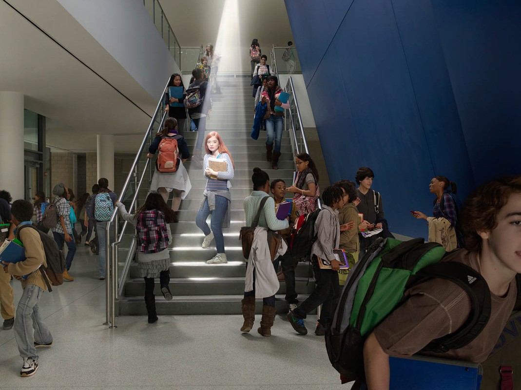Students walk up and down the stairs of a school building, illuminated by a bright light from above in an indoor setting.