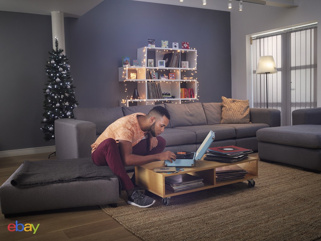 Young man in casual wear uses a vintage record player in a modern living room, surrounded by vinyl records, creating a cozy, retro ambiance.
