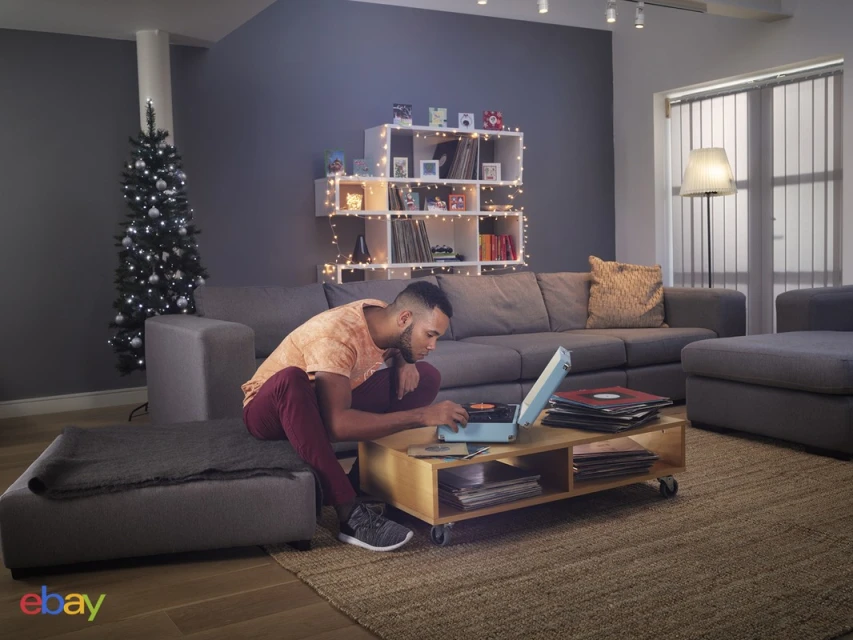 Young man in casual wear uses a vintage record player in a modern living room, surrounded by vinyl records, creating a cozy, retro ambiance.