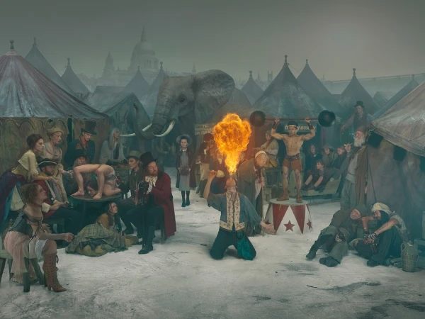 Intricate scene featuring a crowd of circus performers and spectators with an elephant, tents, and a city skyline in the background.