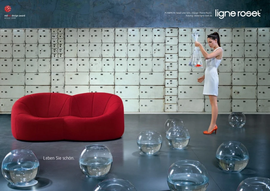 Interior design advertisement: a woman in a white dress holding transparent bags stands near a red sofa and clear glass bowl vases.