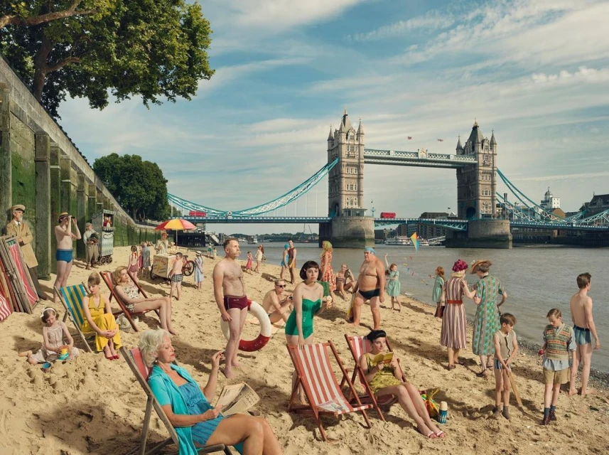 A group of people enjoy a day at the beach in London, with the Tower Bridge providing a unique backdrop to their seaside activities.
