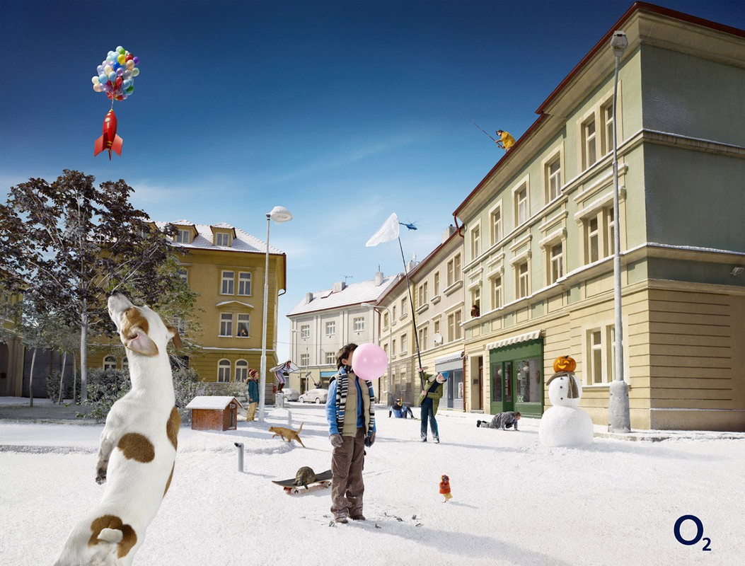 A dog looks up at a balloon-powered rocket in a winter scene, with a boy blowing bubbles in the foreground and people on a snow-covered street.