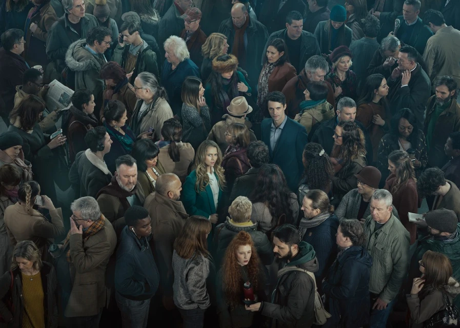 Diverse crowd of men and women, close together, filling the frame with an emphasis on multiple faces and varied clothing styles.
