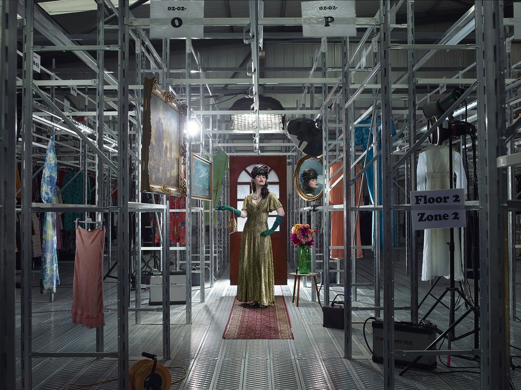 Fashion shot of a woman in a vintage dress in what looks like an indoor industrial setting with shelving, props, and studio lighting.