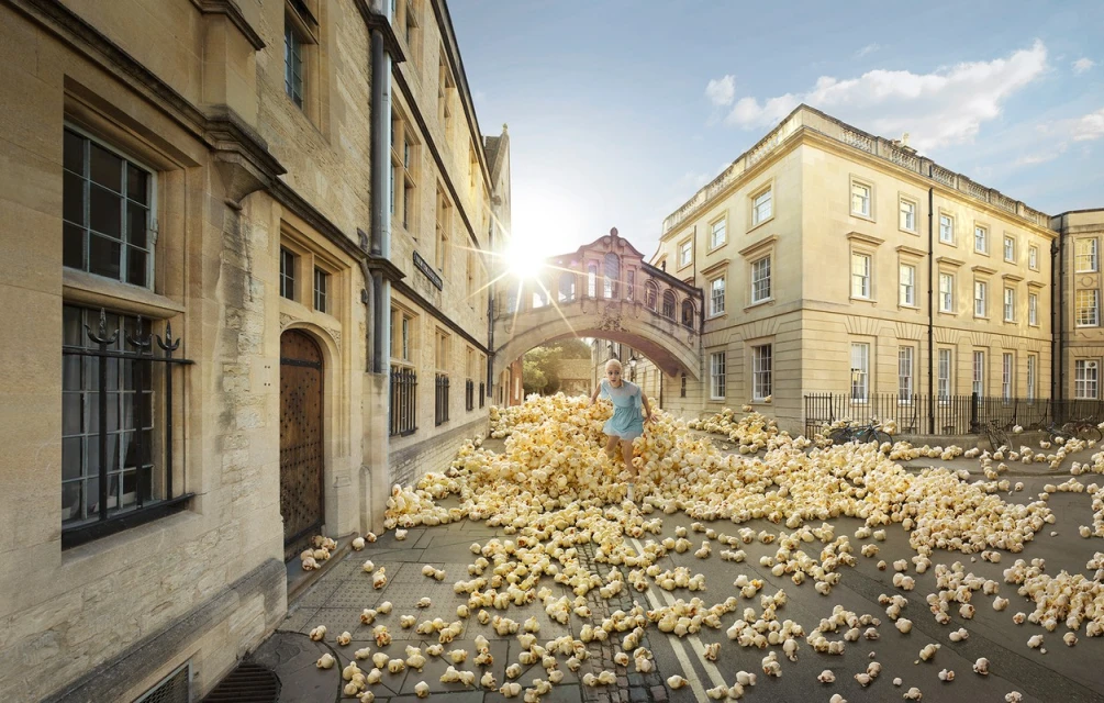 A woman in a blue dress runs across a cobblestone street covered in white balls near the Bridge of Sighs at Oxford University.