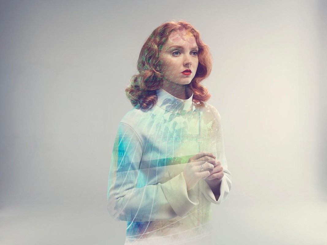Red-haired woman in white turtleneck with double exposure of an abstract landscape with trees and geometric lines in a studio setting.