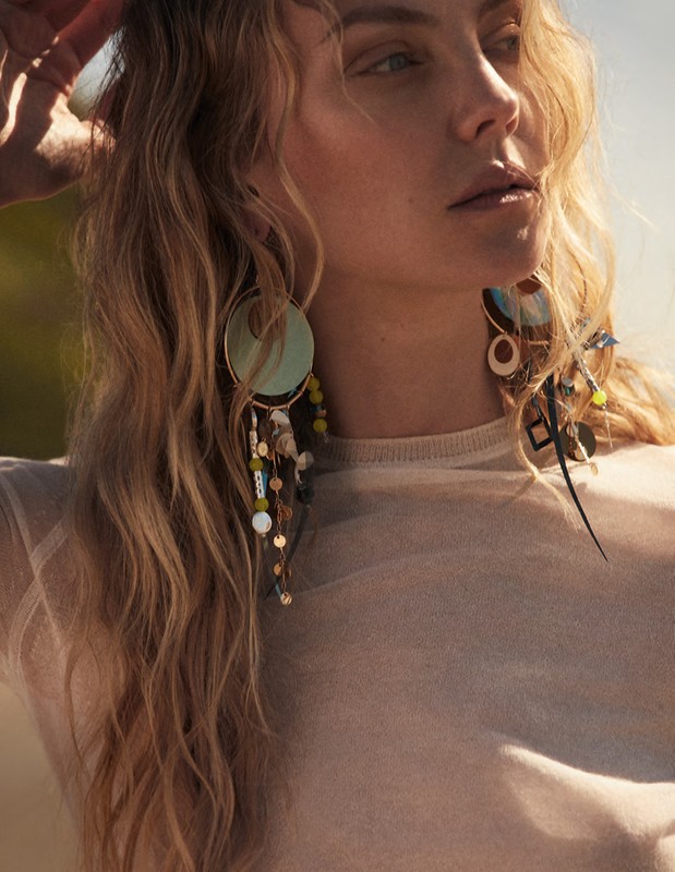 Close-up portrait of a woman with blonde hair wearing large statement earrings and a cream top under natural sunlight.