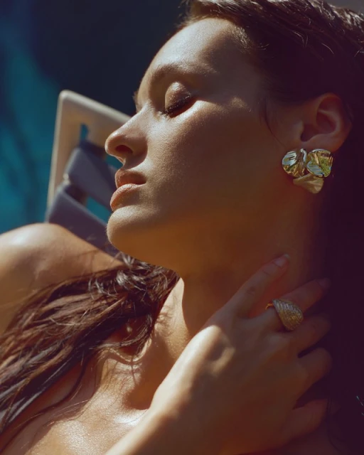 Close-up of a brunette woman with her eyes closed, adorned with jewelry, lying in repose, and bathed in golden sunlight. Beauty shot.