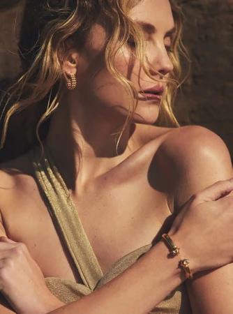 Close-up portrait of a woman with gold hoop earrings and bracelets wearing a sparkling gold dress in natural warm light