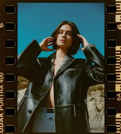 Portrait of a woman with short dark hair wearing a black leather jacket against a clear blue sky and rocky landscape