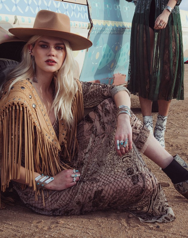 Two women in desert setting wearing vintage clothing, fringe jacket, brown hat, jewelry, snake print boots, in outdoor fashion shot.