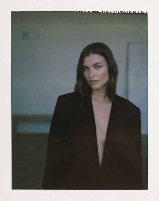 Woman wearing an oversized dark blazer posing against an indoor background with visible polaroid borders.