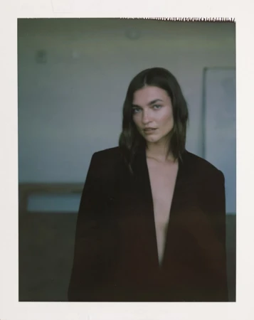 Woman wearing an oversized dark blazer posing against an indoor background with visible polaroid borders.