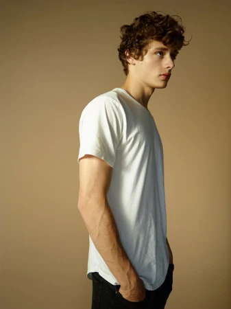 Profile portrait of a young man with curly brown hair wearing a white t-shirt against a plain neutral background.