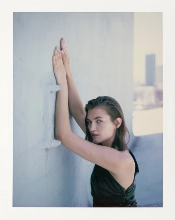 Woman in dark sleeveless top with hands raised against a light wall in Los Angeles