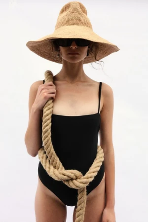 Model wearing a wide-brimmed straw hat, black sunglasses, and a black swimsuit wrapped in thick rope against a plain white background.