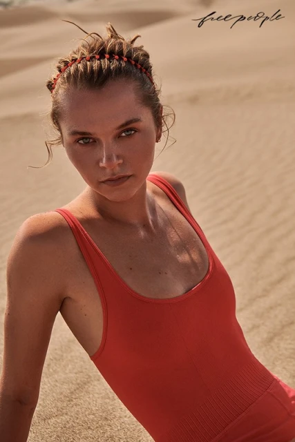 Woman in orange swimsuit poses on sandy dunes for a fashion shoot, featuring neutral color palette, natural light, and the Free People logo.