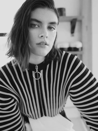 Black and white portrait of a woman with dark wavy hair wearing a striped zip-up top.