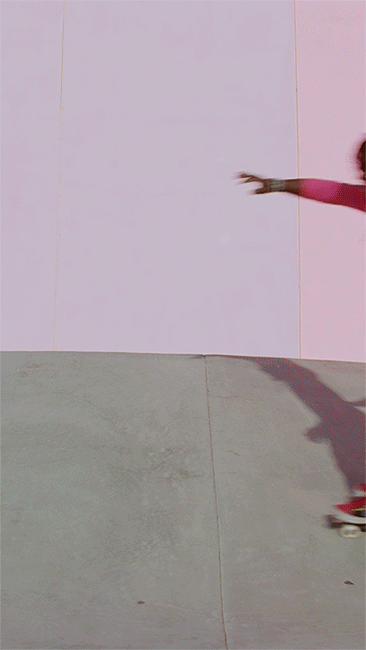 A person wearing pink skateboarding on a grey ramp in front of a two-toned pink wall, creating an interesting vertical composition.