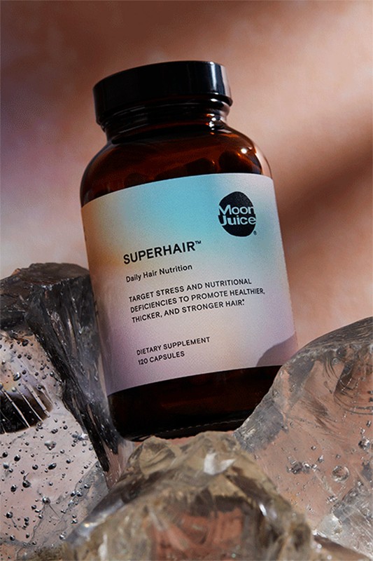 Amber-colored Moon Juice SuperHair bottle with black cap on textured ice. Dietary supplement promotes healthier, thicker hair.