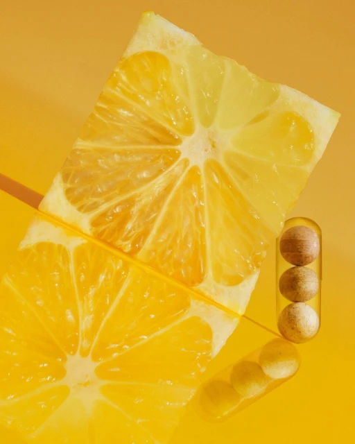 Close-up still life of lemon slices and pills in a clear capsule against a yellow background. Bright, minimalist pharmaceutical concept.