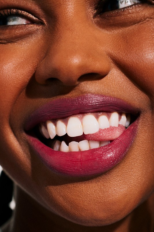 Close-up studio shot of a smiling African American woman with bright white teeth and magenta lipstick sticking her tongue out.