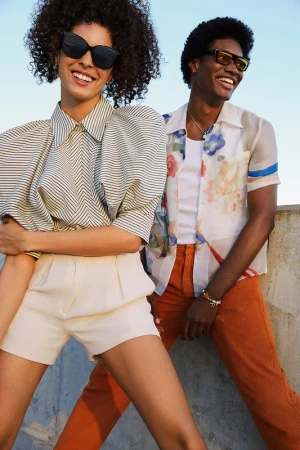 Two smiling models outdoors wearing sunglasses against a clear sky, photographed by Kat Borchart in Los Angeles.