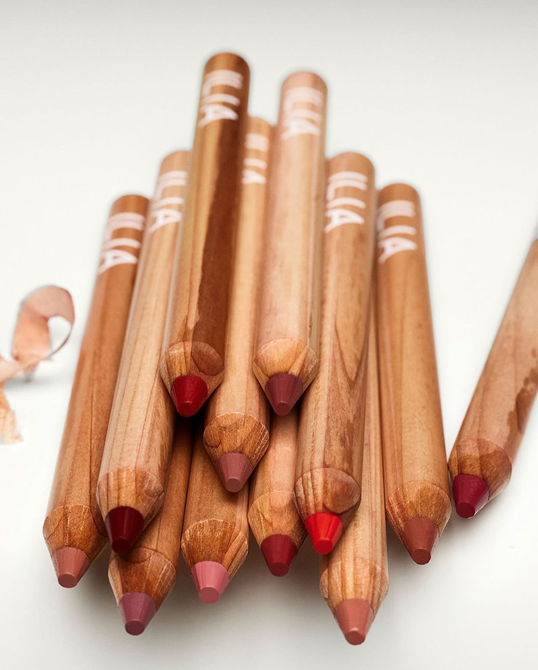 Close-up of wooden lip pencils in various shades of pink and red, arranged in a cluster against a white background. Beauty concept.
