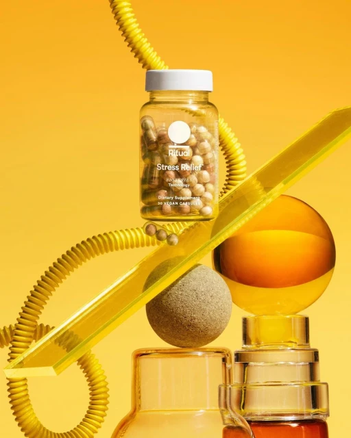 Still life shot of a Ritual Stress Relief supplement bottle surrounded by glass orbs and shapes on a yellow background. Product photography.