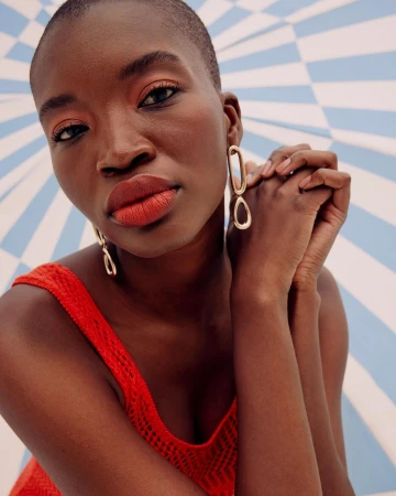 Close-up portrait of a woman with gold earrings against a blue and white striped background, showcasing beauty and minimalist fashion.