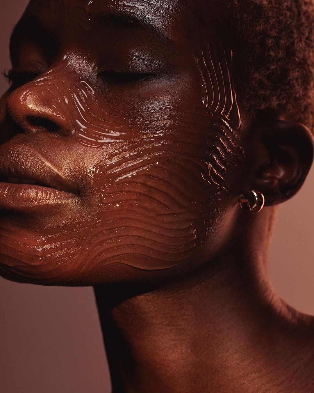 Close-up portrait of a Black woman with glossy gel-like skincare product swatched across her face, by Kat Borchart.