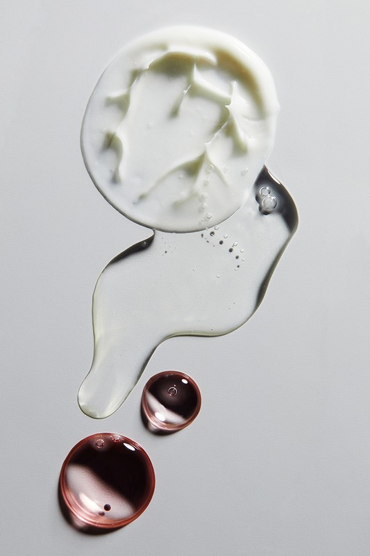 Cosmetic product assortment: a blob of cream, clear gel, and translucent drops on a neutral background in an overhead studio shot.