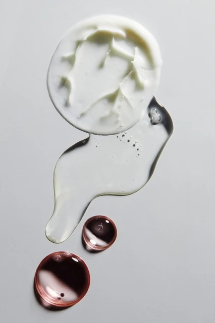Cosmetic product assortment: a blob of cream, clear gel, and translucent drops on a neutral background in an overhead studio shot.