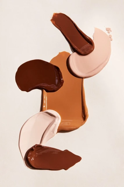 Close-up of cosmetic foundation swatches in different shades of brown and beige, floating on a white background. Beauty product shot.
