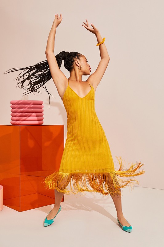 Woman in yellow fringe dress dancing in studio with orange cube and pink pillows, fashion and beauty lifestyle product shot.