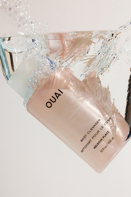 OUAI body cleanser bottle is suspended in clear water with splashes against a white background for a beauty product shot.