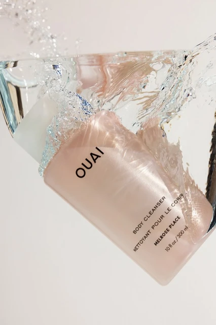 OUAI body cleanser bottle is suspended in clear water with splashes against a white background for a beauty product shot.