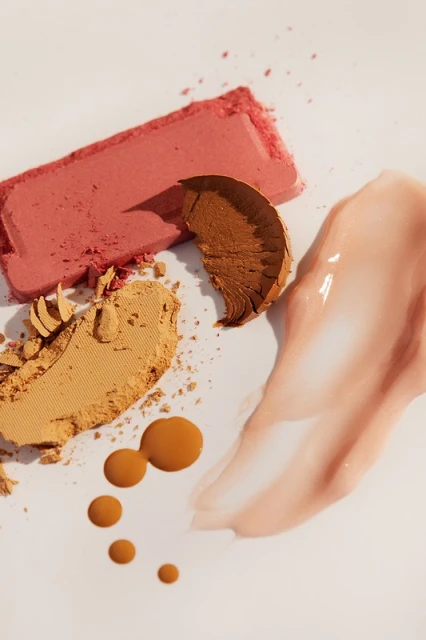 Arrangement of makeup products on a white background. Features blush, bronzer, foundation, and highlighter for beauty and cosmetics.