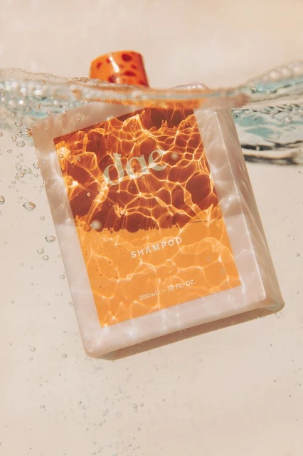 Bottle of daze shampoo submerged in water with bubbles and warm color scheme, focusing on label and refreshing visual.