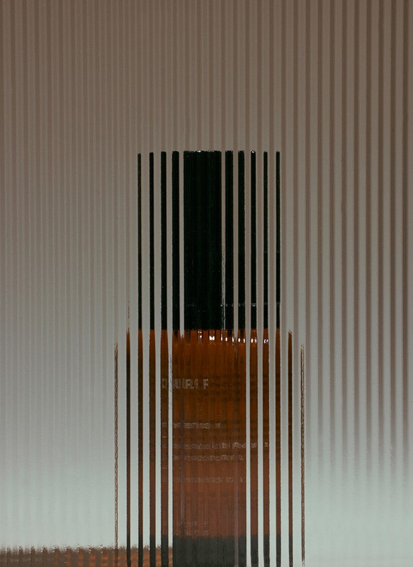 Amber glass bottle with a black cap stands in front of a textured background, creating a minimalist and abstract product shot.
