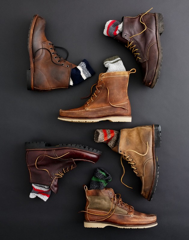 Still-life composition of six arranged brown leather boots with visible socks on a dark gray background, suitable for fall or winter fashion.
