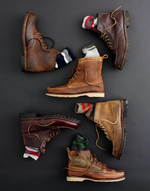 Still-life composition of six arranged brown leather boots with visible socks on a dark gray background, suitable for fall or winter fashion.