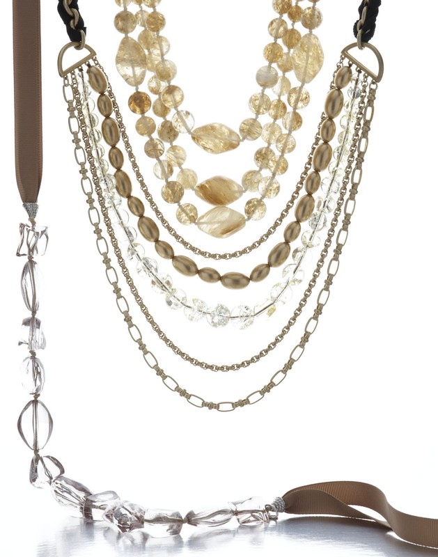 Multi-strand statement necklace featuring gold chains, various tan, gold, and clear beads, and a tan ribbon on a white background.